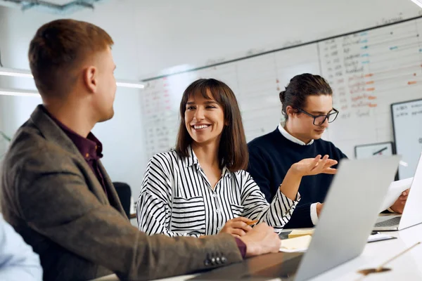 Office worker works with papers while two other workers talk.