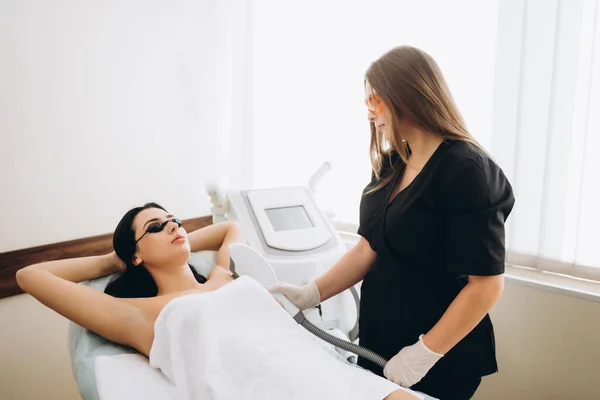 Laser cosmetology armpit hair removal. Beautiful woman client in glasses have fear of pain while doing procedure.