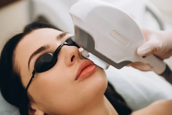 Laser cosmetology armpit hair removal. Beautiful woman client in glasses have fear of pain while doing procedure.