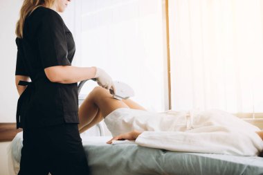 Kız tedavi odasındaki tıbbi gözlüklerle kanepede yatıyor. Kozmetik uzmanının elleri bacakların epilasyonunu yapar..