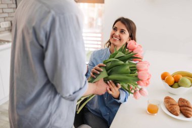 Image of young happy caucasian people, man gives a flowers to his woman at home. Women`s day, Mother`s day