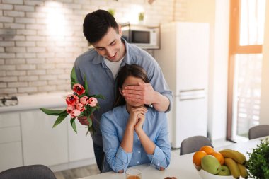 Romantic young man with flowers is covering his girlfriend's eyes. Man wants to make surprise for his girl. Romantic concept