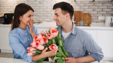 Surprise! Beautiful romantic couple at home. A young man gives flowers to his beloved. A feeling of happiness. Pink tulips
