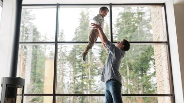 Father and son spending time together, man throwing up his son at home in living room, copy space. Father`s day concept.