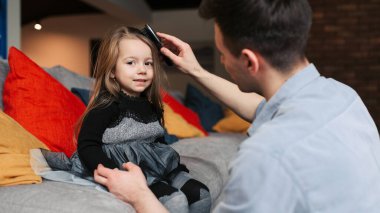 The father helps his daughter to brush the hair. Before going to work and at school, daughter and father spend nice moments