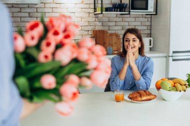 Unexpected moment in routine everyday life! Cropped photo of man's hands holding chic bouquet of pink tulips, happy woman is on blurred background