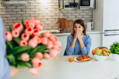 Unexpected moment in routine everyday life! Cropped photo of man's hands holding chic bouquet of pink tulips, happy woman is on blurred background