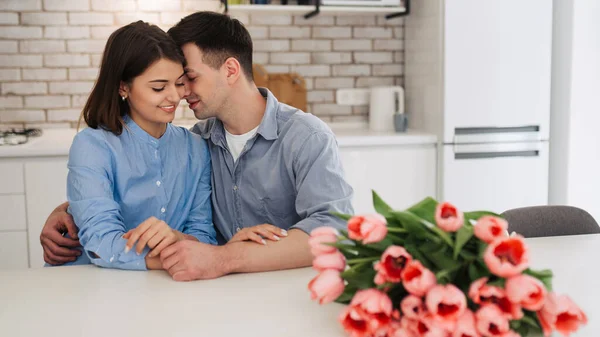 Happy beautiful cute young couple are sitting together on the kitchen with flowers. Love, celebration, romantic, st. Valentine\'s day, women day, birthday, date.
