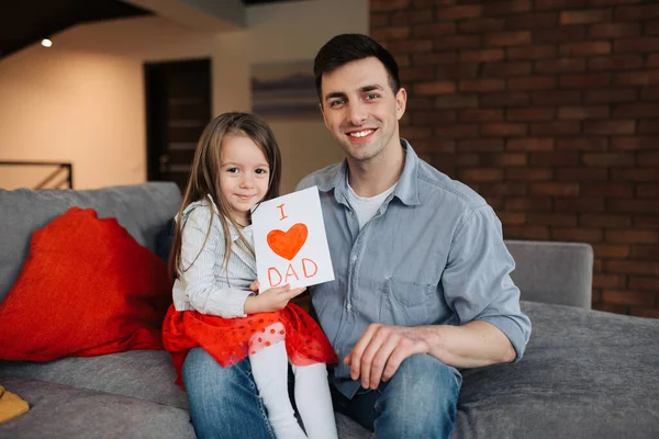 I love you, dad! Handsome young man at home with his little cute girl. Happy Father\'s Day. The daughter sits on her father\'s lap and congratulates him on Father\'s Day.