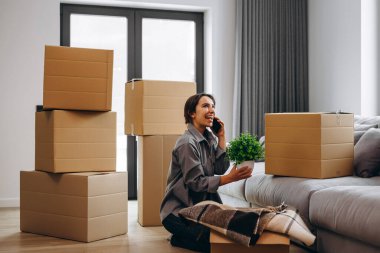 A happy female homeowner is unpacking a parcel with things from a transport company and talking on the phone. Delivery service, moving to a new house
