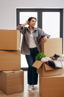 Young woman smiling confident standing at new home. Single lady moves. Real estate purchase, mortgage, delivery service ordering concept.