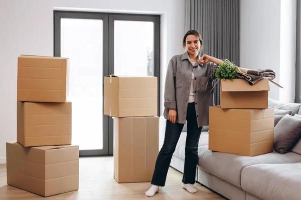 A young girl moved to a new house. happy looking at the camera on the background of many boxes. Dream come true! Portrait of young pretty woman sitting on the floor and thinking how to unpack all the stuff.