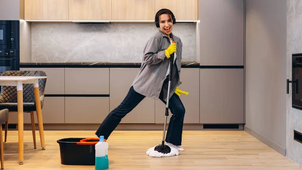 Happy student or business woman cleaning home, singing using mop like microphone and having fun while she wipes the floor. Young female doing housework, chores concept