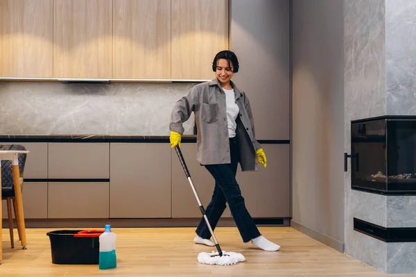 Happy student or business woman cleaning home, singing using mop like microphone and having fun while she wipes the floor. Young female doing housework, chores concept.