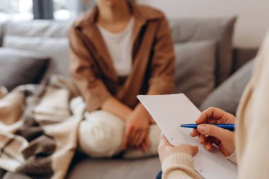 Young sad woman is sitting on the couch, holding her hands to her face at a psychotherapist's appointment. Psychologist with a client