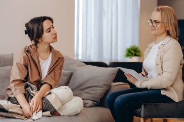 Young sad woman is sitting on the couch, holding her hands to her face at a psychotherapist's appointment. Psychologist with a client