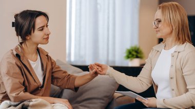 Psikolog randevusunda tatlı bir kız. Psikolog kadın hastasının elini tutuyor. Aile sorunları, ergenlik sorunları. Bir terapistle konuşmak, tavsiye, yardım kavramı.