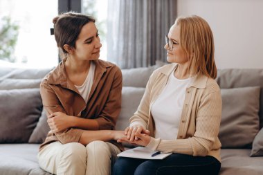 The girl came for a consultation with a psychologist, the psychologist and the client look at each other, and the psychologist holds the client's hand in a gesture of support.