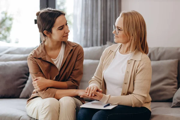 The girl came for a consultation with a psychologist, the psychologist and the client look at each other, and the psychologist holds the client's hand in a gesture of support.