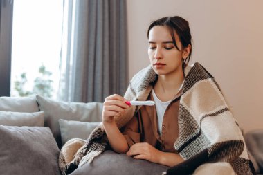 A sick, sad girl has a high temperature, a sore throat and a runny nose. She feels very bad.