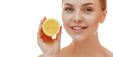 Close up shot of nice looking young woman touches face gently has well cared complexion healthy glowing skin stands bare shoulders holds half of juicy lemon isolated over white studio background.