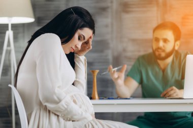 Hamile kadın masada otururken baş ağrısı çekiyor..