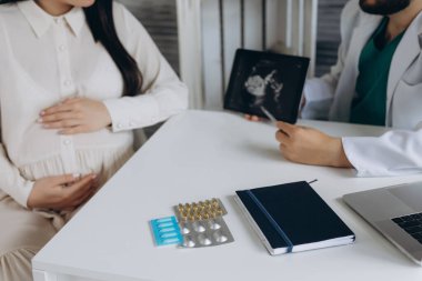 Doktor hamile bir kızın ultrasonunu gösteriyor. Klinikteki doktora geldi. Bir jinekolog. Beyaz bir bornoz giymiş..