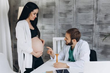 Klinikte hamile bir kadınla çalışan kadın jinekolog. Doktor hastanın kalp atışlarını dinliyor..