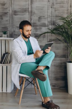 Gülümseyen genç bir pratisyen hekimin portresi ya da beyaz üniformalı ve gözlüklü bir doktor hastanede poz veren kameraya bakın..