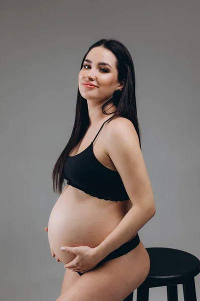 妊娠中の女性は彼女の腹に触れ 灰色の背景にポーズ — ストック写真