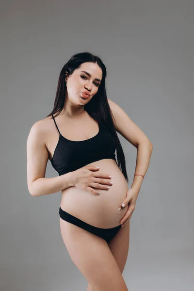 妊娠中の女性は彼女の腹に触れ 灰色の背景にポーズ — ストック写真