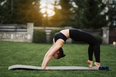 Dışarıda yoga yapan bir kadın. Vücut giysisi giyen genç, çekici, zayıf fitness kızı dinleniyor ve egzersiz yapıyor.