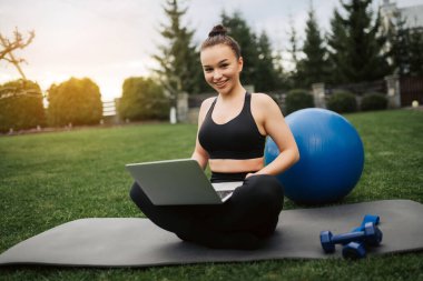 Mutlu gülümseyen kadın karantina sırasında bahçede meditasyon yapıyor. Skype üzerinden rehberlik veya çevrimiçi öğretim veya eğitmen talimatları doğrultusunda evde meditasyon ve rahatlama