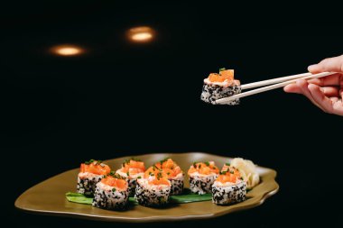 Somon, salatalık, avokado, krem peynir, tobiko havyar, baharat sosu, Çin yemek çubuğunda susam, masanın üzerindeki tabağın üstünde.