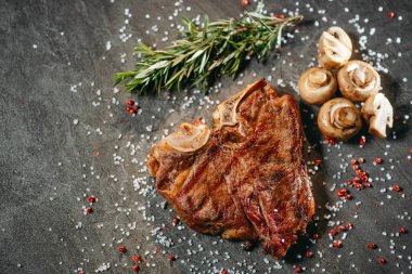 Sulu ve ızgara et parçası tuzlu ve biberli bezelyelerin üzerine serpilmiş, biberiye filizi yanında ve profesyonel bir mutfakta taş bir masada pişirilmiş mantarlar.