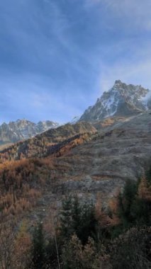 Güneş ışığı, renkli bir sonbahar ormanının arkasındaki Mont Blanc bayırlarını yavaşça aydınlatır. Chamonix, Fransa Kasım 'da