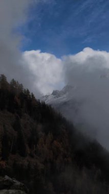 Fransa 'nın Chamonix kentindeki bir ormanın yakınındaki karlı dağ tepelerinin üzerinden geçen beyaz bulutlar Kasım ayında Les Houches' da