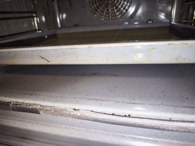 Ev fırınının içinde oturmuş yağlı ve kirli yemek tepsisi, eksiksiz bir temizlik ihtiyacını gösteriyor.