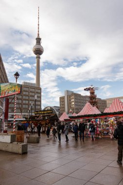 Berlin, Almanya - 15 Aralık 2019: İnsanlar İskender Meydanı 'nda arka planda televizyon kulesi olan geleneksel ahşap kulübelerde Noel ruhunun keyfini çıkarıyorlar