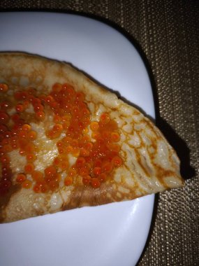 Thin folded crepe topped with glistening red caviar, served on a white plate