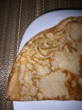 Katlanmış bir krepin kapağı, altın kahverengi dokusunu gözler önüne seriyor, örülmüş bir paspasın üzerinde beyaz bir tabakta servis ediliyor.