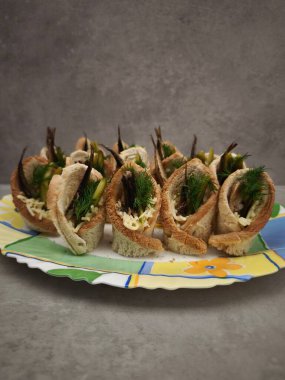 Dereotu ve turşuyla süslenmiş küçük balık kanapeleri renkli bir tabakta servis edilir, aperatif olarak noel kutlaması için mükemmel parti yemekleri, yeni yıl yemeği, Noel ya da doğum günü yemeği