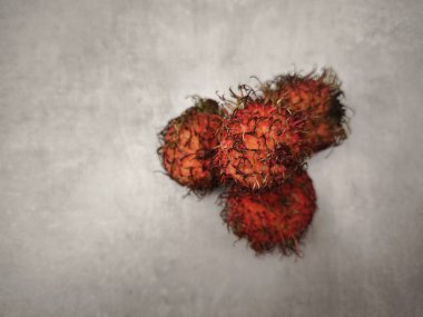 Birkaç olgun rambutan meyvesi gri bir yüzeye yerleştirilir, canlı kırmızımsı renkleri ve karakteristik kıllı dış görünüşleri sergilenir.