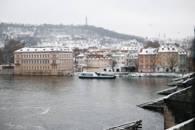 Prag, Çek Cumhuriyeti - 22 Ocak 2023: Vltava Nehri, tekne, karlı setler, renkli binalar ve kışın Petrin Tepesi manzarası. Yüksek kalite fotoğraf