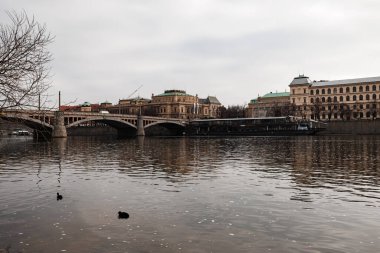Prag, Çek Cumhuriyeti - 4 Mart 2023: Bulutlu bir günde arkaplanda köprü, Marina restoranı ve diğer tarihi binalarla Vltava nehrinin manzarası