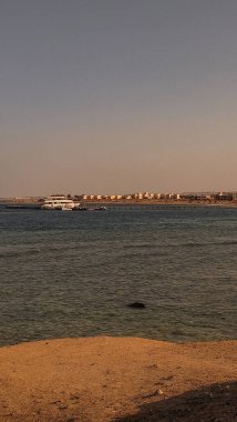 Kızıl Deniz 'in kumlu bir plajla buluşmasının sakin bir sahnesi, Marsa Alam, Mısır' da berrak bir gökyüzünün altında görünen bir tatil köyü.