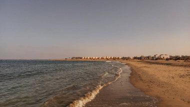 Sakin dalgalar Marsa Alam, Mısır 'ın kumlu plajını yıkıyor. Arka planda tatil köyü binaları gün batımında.