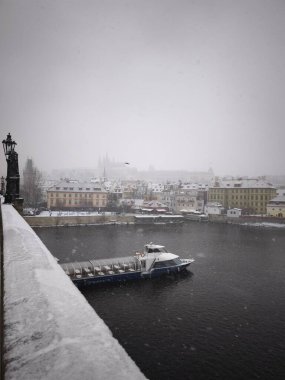 Prag, Çek Cumhuriyeti - 5 Ocak 2025: Vltava nehrinin üzerine kar yağıyordu, nehir kıyısı ve sisli arka planda görünen tarihi binalar ile birlikte.