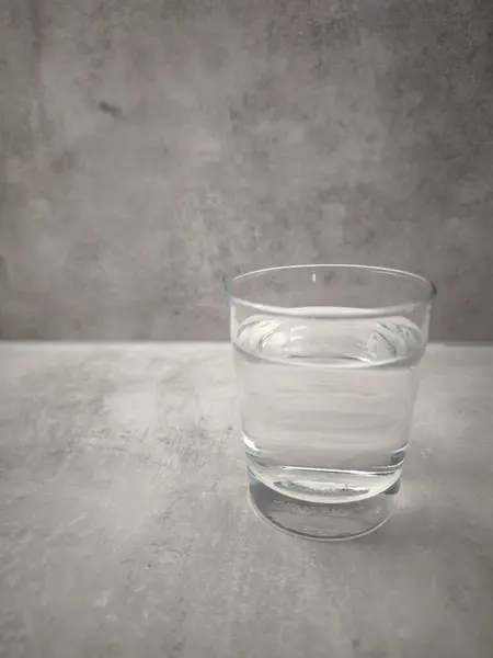 Prag, Çek Cumhuriyeti - 1 Ocak 2025: Su şeffaf Ikea bardağını doldurdu, pürüzsüz beton zemin üzerinde dinleniyor, temiz tasarımın minimalist estetiği. Sağlığın sembolü. Dünya Su Günü kopyalama alanı