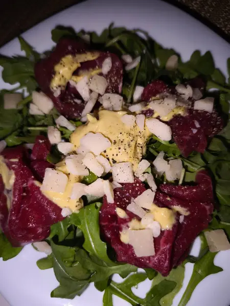 İnce dilimlenmiş çiğ sığır carpaccio biberli roka üzerinde dinleniyor, üzerine parmesan serpiştirilmiş lezzetli hardal sosu serpiştirilmiş, Prag 'da fotoğraflanmış. Parti, açık büfe ve şık aperatifler için idealdir.